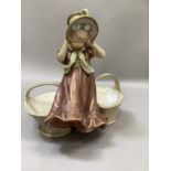 A Royal Dux Bohemia figure, a girl holding onto her bonnet in the wind, flanked by a basket to