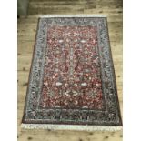 A Persian style cashmere and silk rug of red ground and all over plant form design within a main