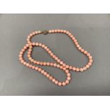A coral necklace of spherical beads fastened with a drum snap pierced with Chinese characters in