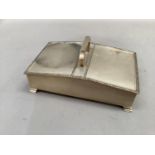 A silver cigarette case having twin hinged lids and central carrying handle on bracket feet, all