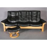 A Stressless black leather and beech reclining three seater sofa with matching footstool