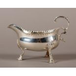 A GEORGE III SILVER SAUCE BOAT with a punchwork rim, acanthus scroll handle and on three hoof