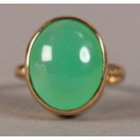 A JADE DRESS RING IN 9CT GOLD, the oval cabochon stone collet set and raised against a plain