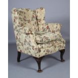 A GEORGE III STYLE MAHOGANY WINGED ARMCHAIR upholstered in floral fabric, scroll-over arm,