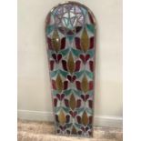 A leaded coloured glass panel of arched profile in clear, pale yellow, red and turquoise glass,