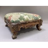A Victorian walnut footstool of square outline having a foliate carved and C-scroll apron on claw