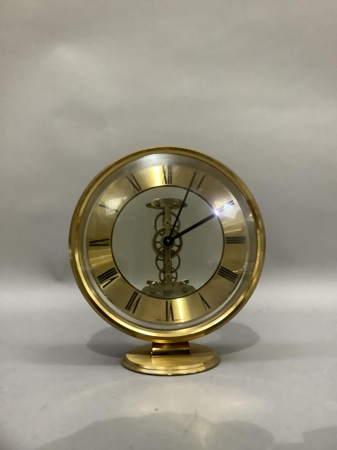 An Acctim gilt metal mantel clock with exposed quartz movement, circular chaptering with black Roman