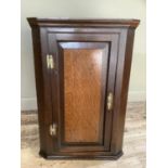 A 19th century oak corner hanging cupboard having a panel indented door with H brass hinges and