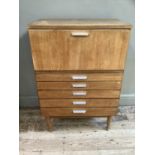 A early 1970s teak cabinet having a drop front over five graduated drawers all with aluminium bar