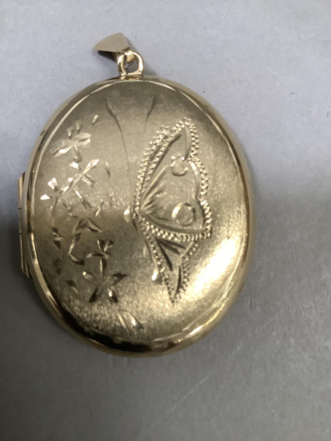 A locket in 9ct gold of oval outline, engraved to the front with a butterfly and foliage against a