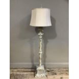 A cream metal standard lamp on a square base with tied leaf terminal with a pale Cognac shade
