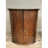 A George III oak bow fronted two door hanging corner cupboard