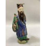 A pottery figure of a china man glazed in blue, green and brown, standing upon a raised base, 25.5cm