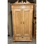 A pine wardrobe having an urn pediment over two doors and drawer below, on bun feet, 202cm high,