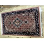 A Middle Eastern rug of salmon ground with central medallion within a dark blue patterned border,