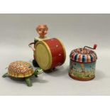 Three printed tin plate toys including a circus drummer, a clockwork tortoise and a music box.