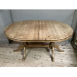An oval pine extending dining table on twin pedestal supports