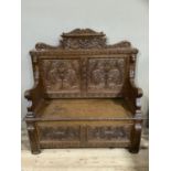 A Victorian carved oak settle having a raised back carved with fruit and foliage above two panels