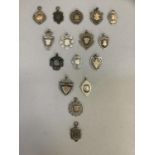 A collection of 16 early 20th century silver shield shaped watch chain medallions, total approximate