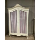 A cream finished French style armoire having an arched moulded cornice above two glazed doors, swept