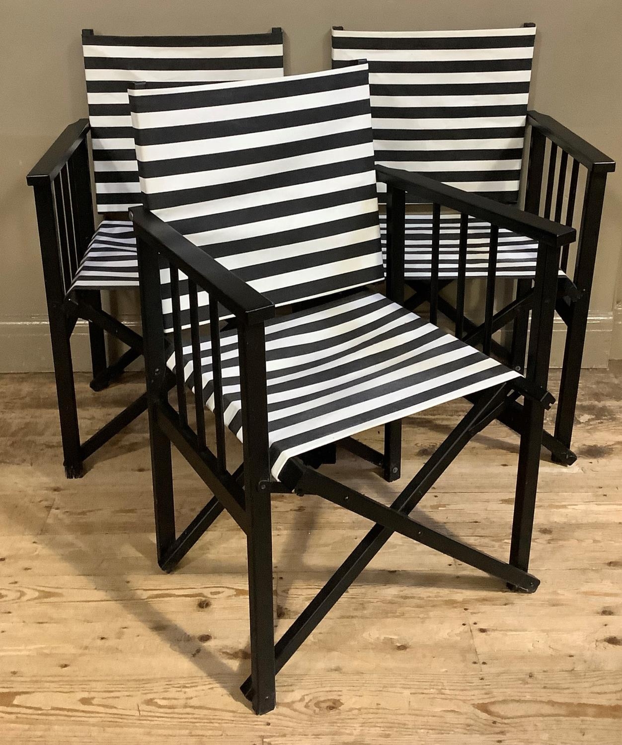 A set of three black framed director's chairs with black and white striped fabric seating