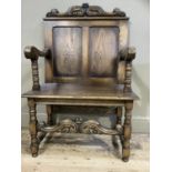 An oak chair having a scroll and foliate carved cresting rail over a twin indented panel back,