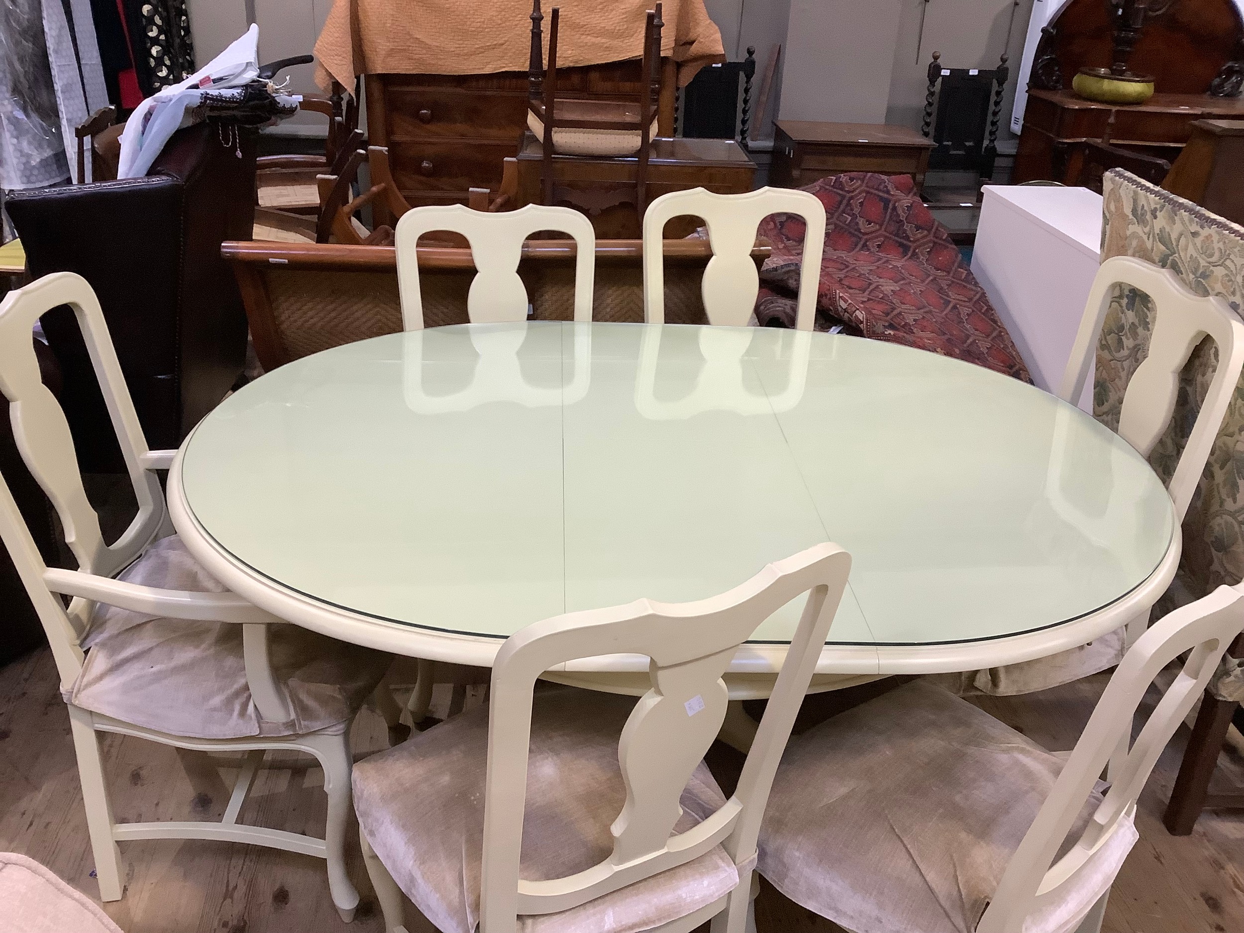A cream finished dining table and six chairs, the table of oblong form and a quadruple pedestal