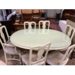 A cream finished dining table and six chairs, the table of oblong form and a quadruple pedestal