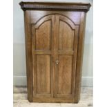 A 19th century oak hanging corner cupboard having two arched indented panel doors with cross banding