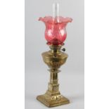 A VICTORIAN BRASS OIL LAMP HAVING A CRANBERRY GLASS SHADE, writhen embossed reservoir above a square