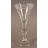 AN ENGRAVED BALUSTER WINE GLASS, the flared bowl with a formal scroll border finely engraved above