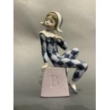 A Lladro figure of a harlequin sat upon a box incised with a letter B