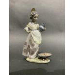 A Lladro figure of a Spanish girl holding a jug on her hip, a seafood paella cooking on a fire at