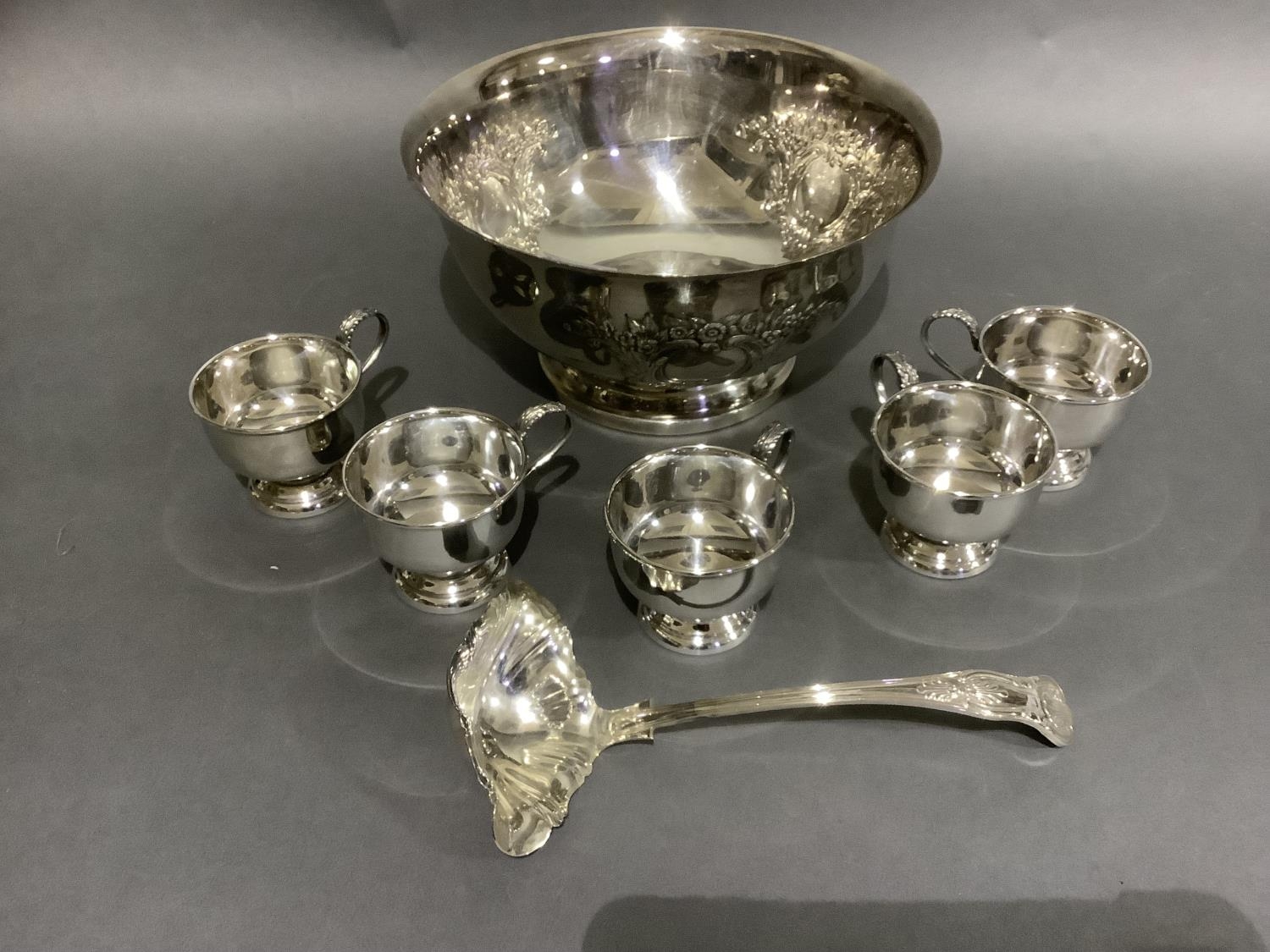 A good silver plated punch bowl with six cups and ladle, embossed with flowers and blind cartouche,