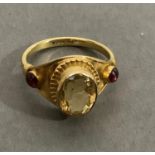 A citrene and garnet ring in 9ct gold, the oval faceted citrene collet set, raised against and
