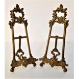 PAIR OF SMALL GILT METAL EASELS with scroll decoration and a fixed rear support leg, 24cm high (2)