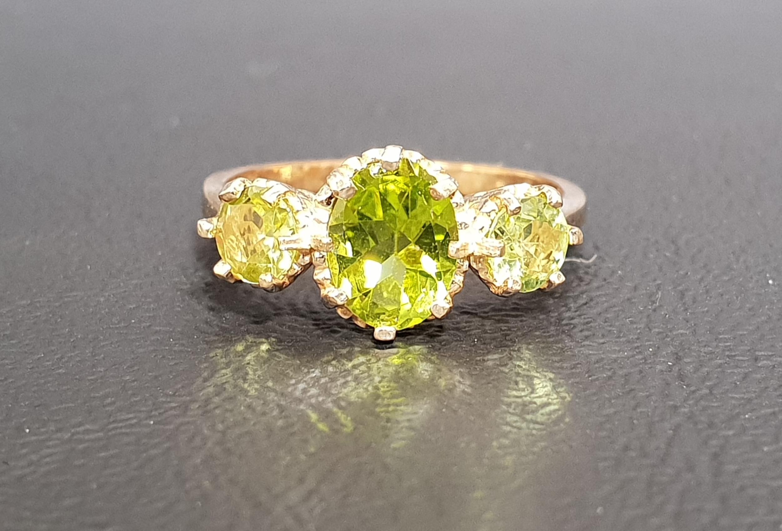 GRADUATED PERIDOT THREE STONE RING the central oval cut peridot approximately 1.2cts flanked by