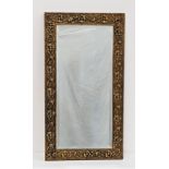 BRASS EMBOSSED WALL MIRROR decorated with flowers around a bevelled plate, 71.5cm high