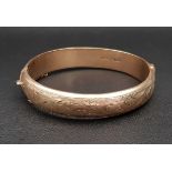 NINE CARAT GOLD HINGED BANGLE with engraved scroll detail and safety chain, approximately 22.2
