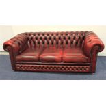 CHESTERFIELD SOFA in ox blood red leather with a button back and scroll arms with decorative stud