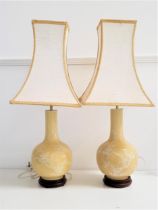 PAIR OF CHINESE STYLE BOTTLE LAMPS with a pale yellow ground and decorated with birds in a tree,