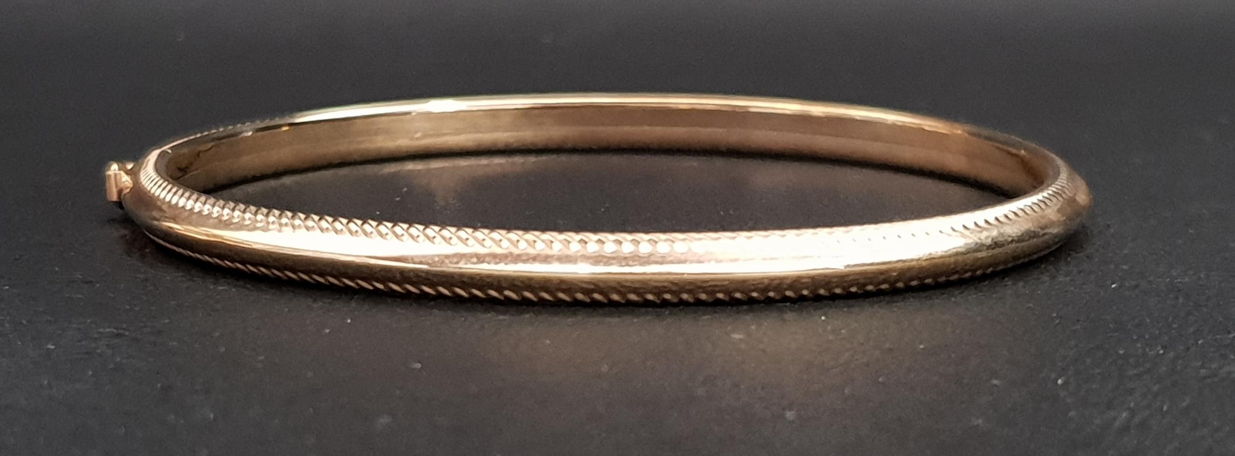 NINE CARAT GOLD BANGLE with ribbed edge detail and safety clasp, approximately 4.3 grams