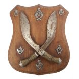 Two crossed Gurkha Kukris and six Gurkha badges mounted on a hardwood shield, 15" (38cm) high, 13"