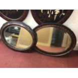 Two oval rosewood effect bevelled wall mirrors with beaded detail and carved edges, the largest