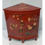 A 20th century Oriental red lacquered standing corner cupboard with a pair of doors decorated with