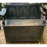 An 'antique' oak box settle, with panelled back and front, scrolled arms, hinged box seat and base