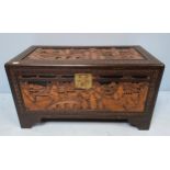 A Chinese camphor lined trunk, carved to the top and front with scenes of figures amidst bridged,