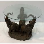 A heavily carved circular wooden coffee table with glass top, depicting three elephants with