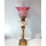 A brass oil lamp with classical column base, clear cut-glass reservoir and etched cranberry shade,