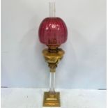 A Lampe Belge Patent 11285-1884 brass and glass oil lamp, with cranberry glass shade, raised on a